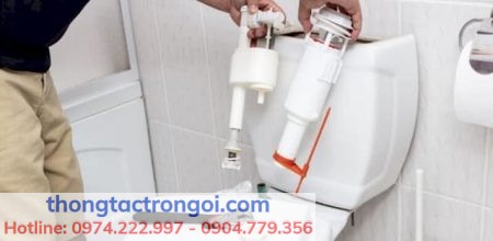 Một bồn cầu với nước rò rỉ, nền sáng, kèm bộ xả bị hư đang được tháo ra