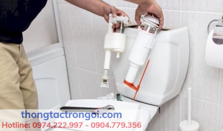 Một bồn cầu với nước rò rỉ, nền sáng, kèm bộ xả bị hư đang được tháo ra