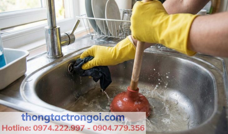 Người dùng đeo găng tay sử dụng cây thụt bồn rửa bát và bịt lỗ thoát tràn để tạo áp lực nén khí tối đa.