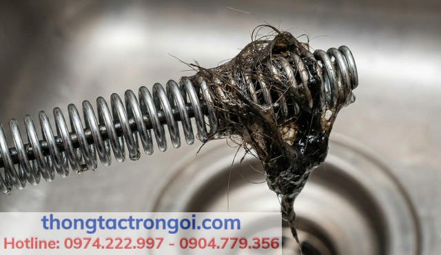 Cận cảnh đầu dây lò xo xoắn ốc của dụng cụ thông tắc đang móc được tóc rối và rác thải từ đường ống.